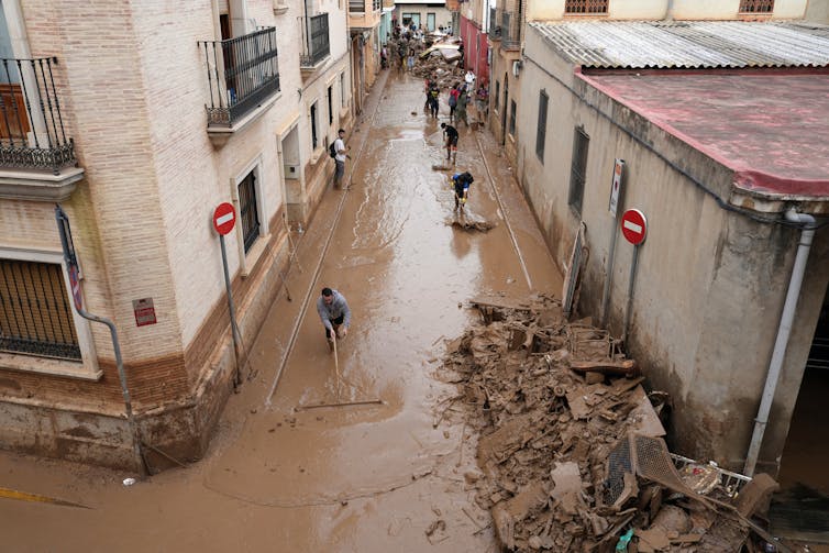 People trying to drag mud on a street full of debris after Spain's worst floods in a generation.
